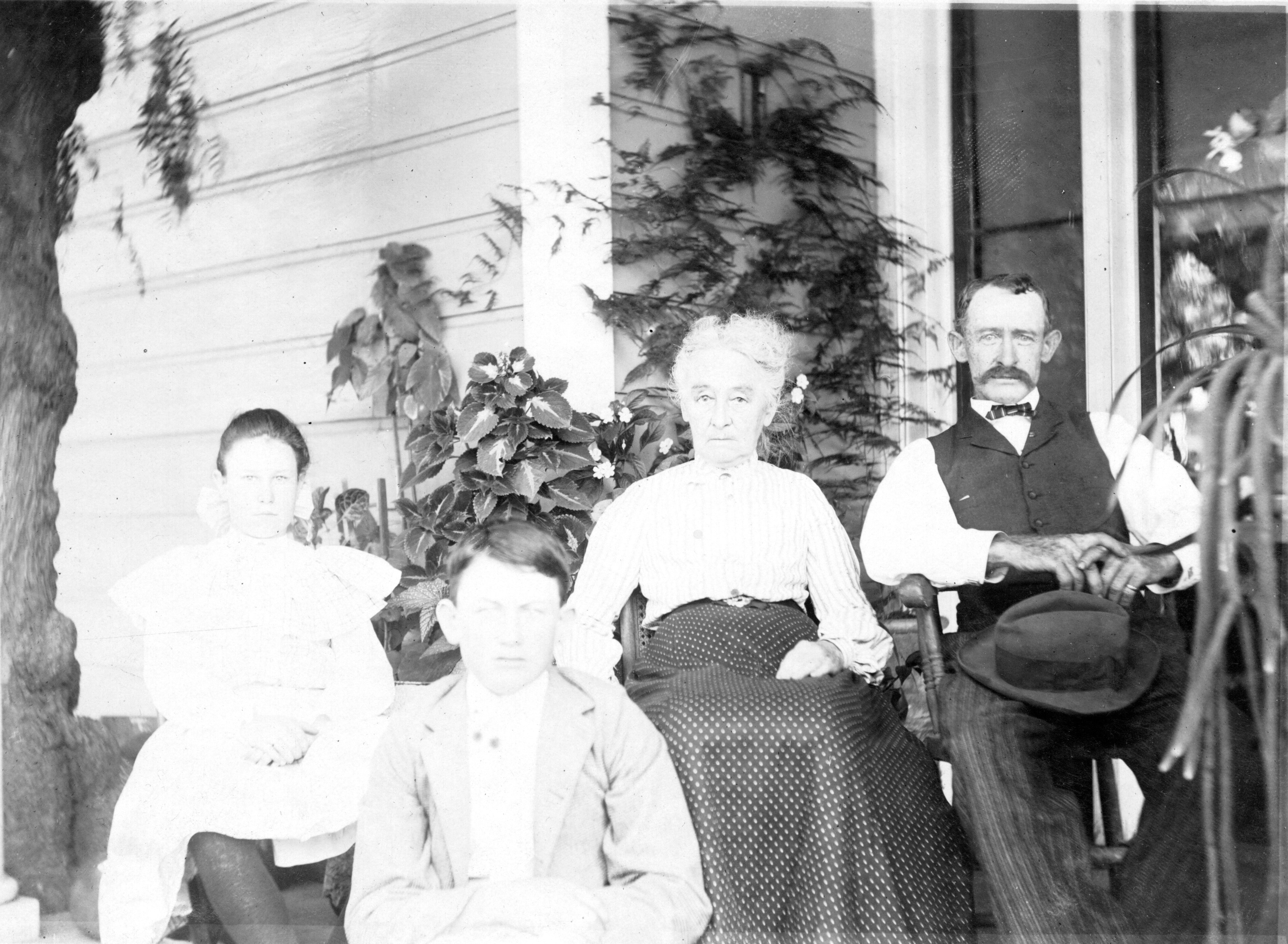 A black and white photograph of the Des Granges Family sitting on the east porch of the house in 1902.
