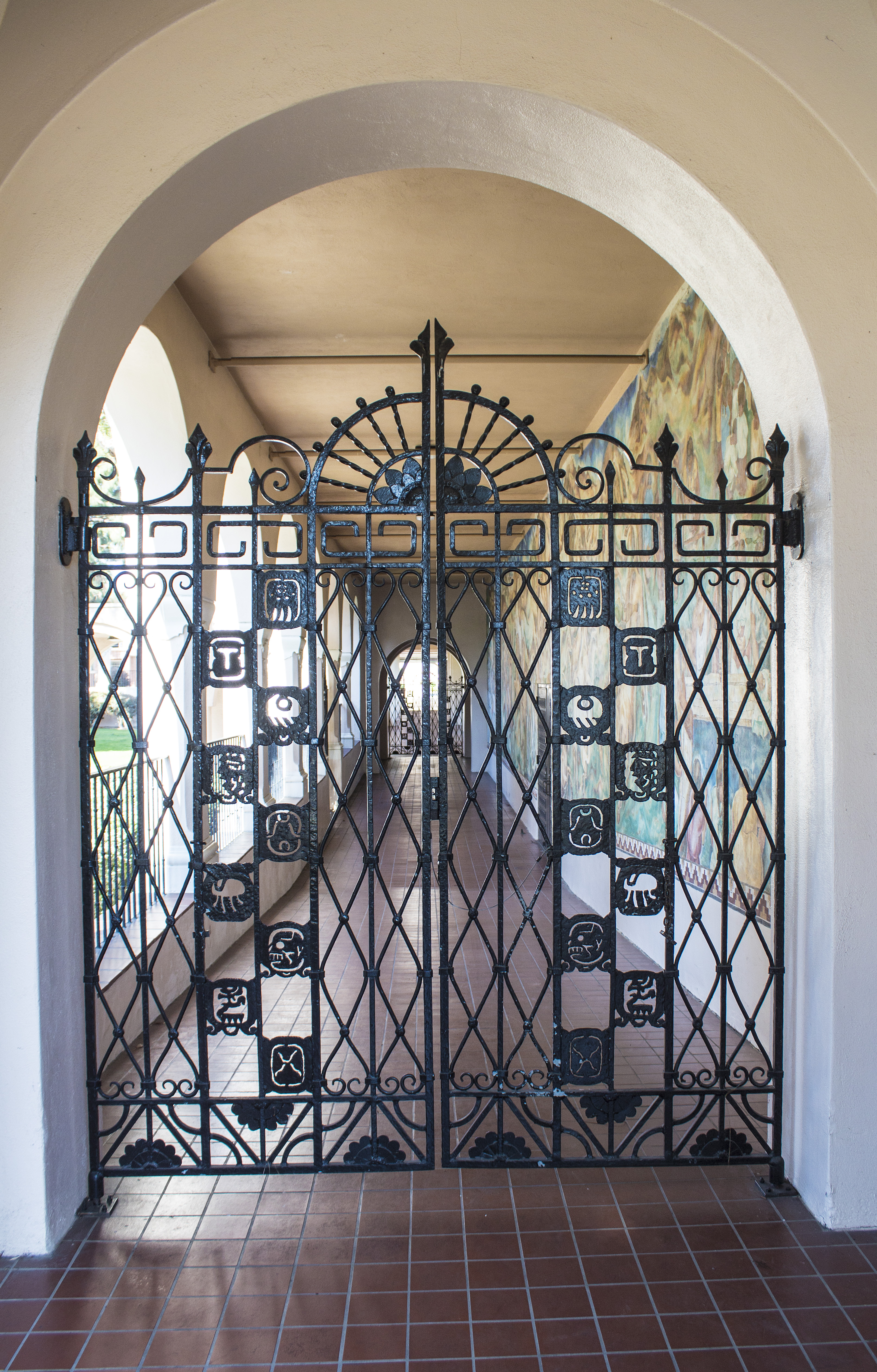 A colored photo of the Mayan Revival wrought-iron gate next to the &quot;Pastoral California&quot; Mural.