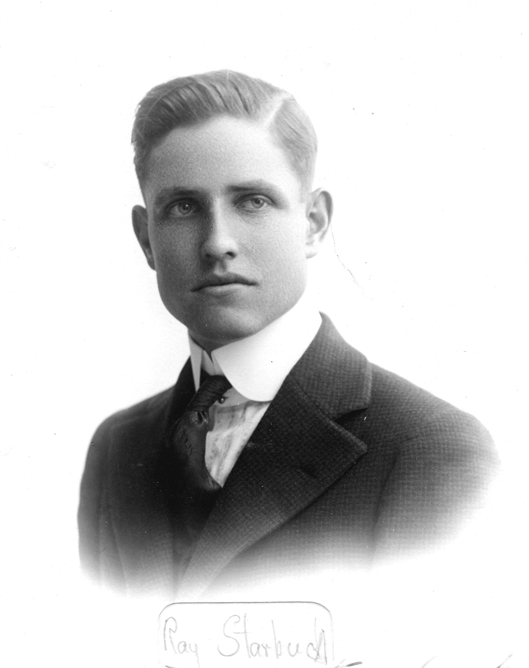 A black and white portrait photograph of Raymond Starbuck. The bottom of the photo is handwritten: Ray Starbuck.
