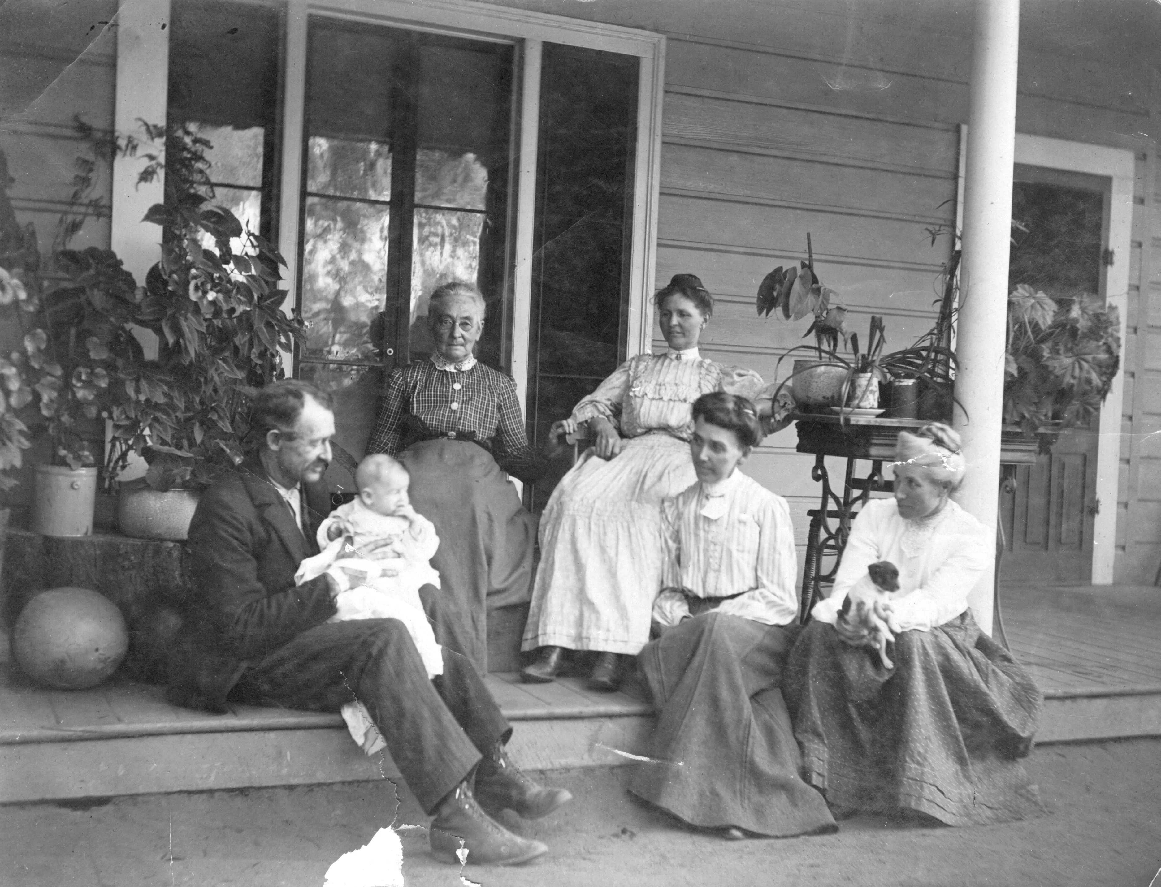 A black and white photograph of the Des Granges family sitting on the back porch of the house in 1891.