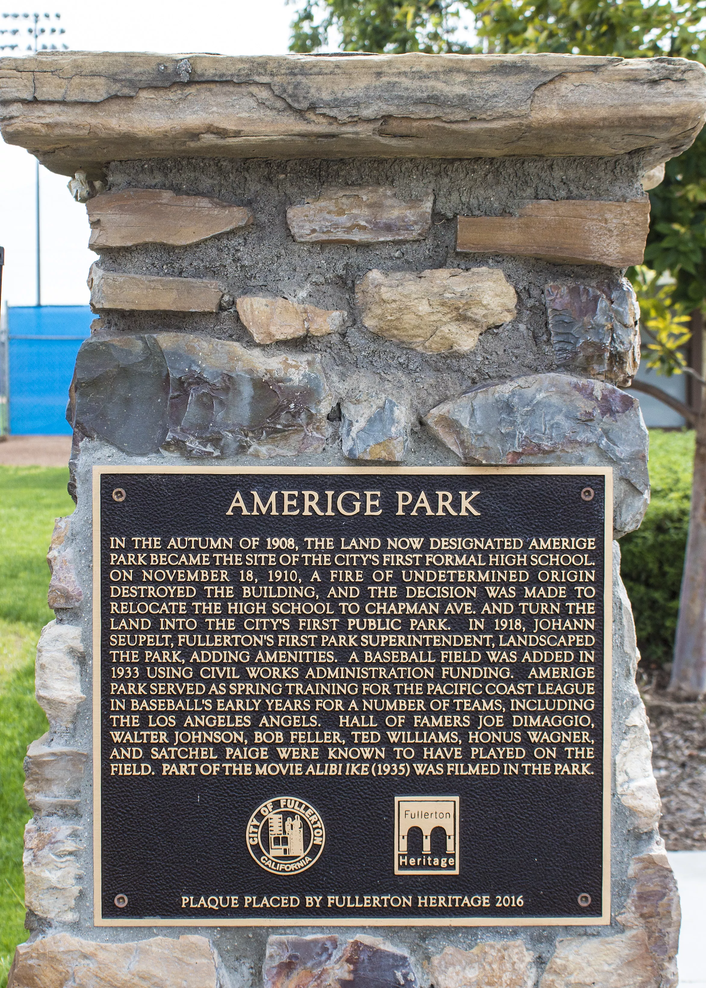 A colored photo of one of the stone pilasters at Amerige Park in 2017. The plaque on the pilaster details various historical facts about the history of Amerige Park. The bottom of the plaque reads: Plaque placed by Fullerton Heritage 2016.