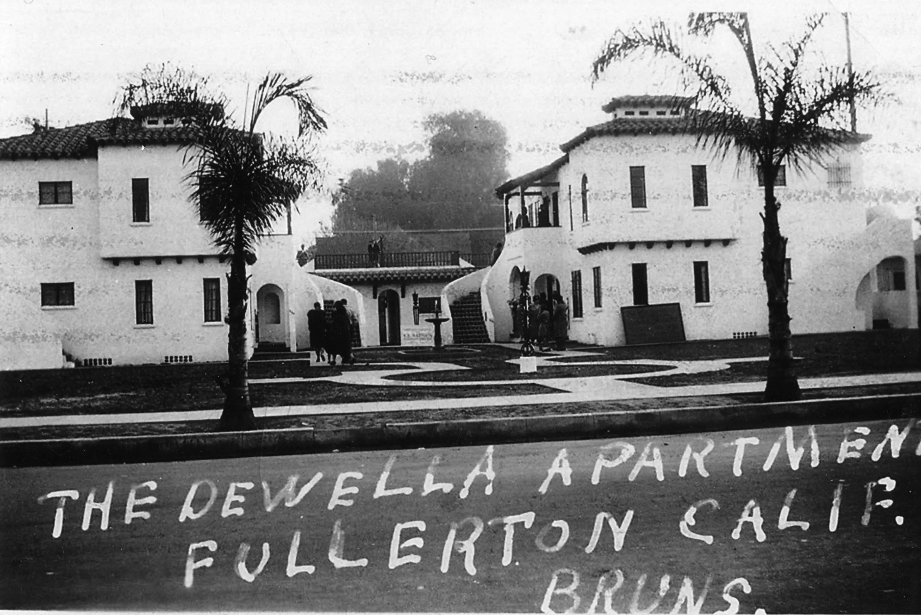 A black and white photograph of the exterior of the Dewella Apartments in 1929. The bottom portion of the photo is handwritten: The Dewella Apartments. Fullerton, California. Bruns.