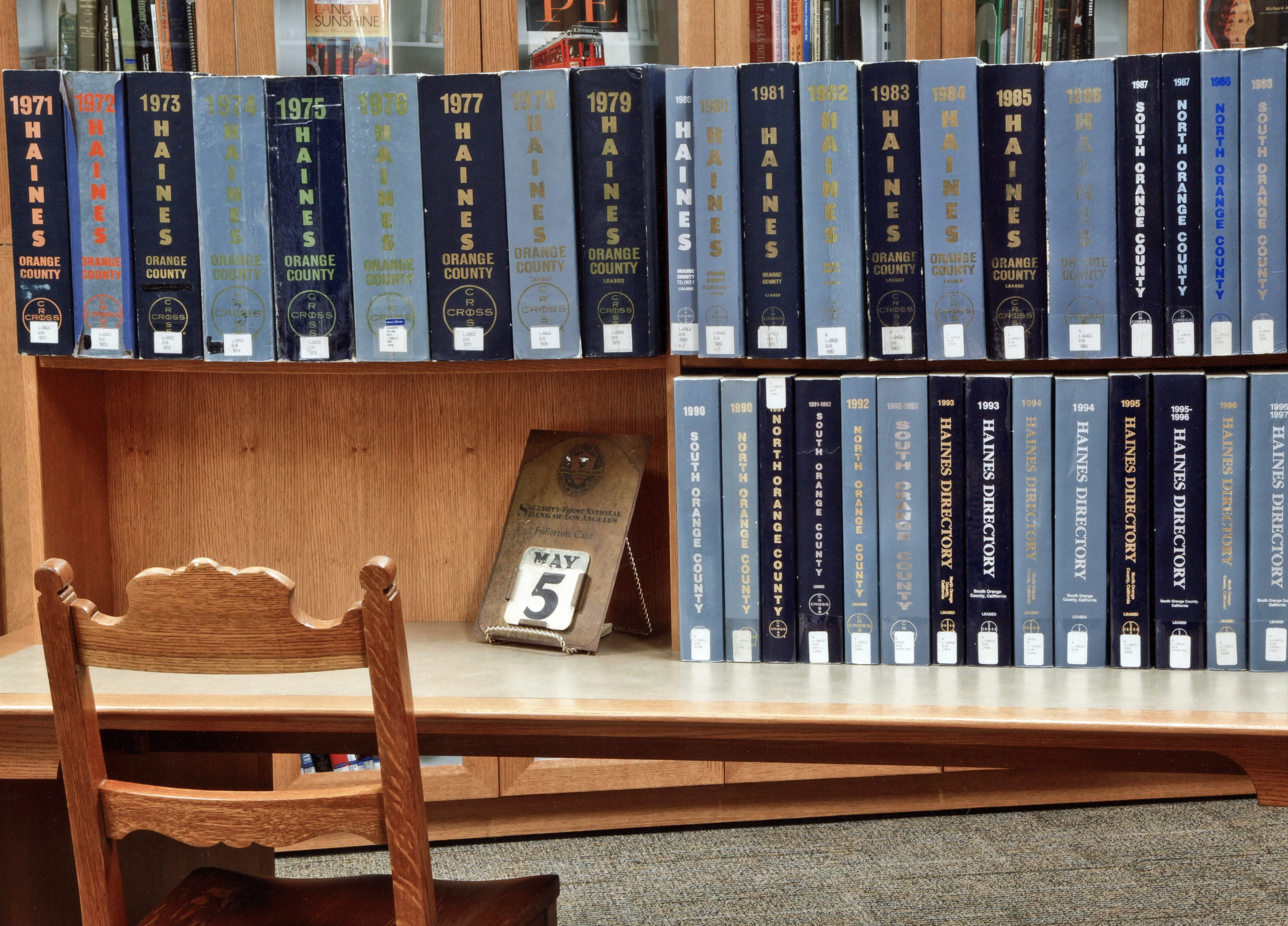 A colored photo of a shelf table inside the Local History Room filled with shelves of Orange County directories.