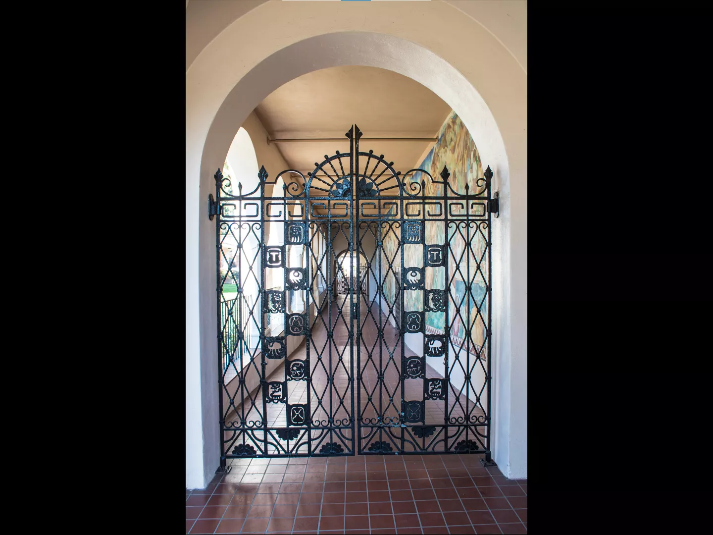 A colored photo of the Mayan Revival wrought-iron gate next to the &quot;Pastoral California&quot; Mural.