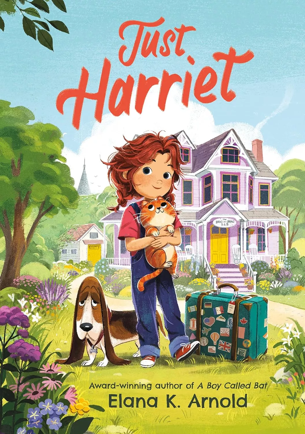 Cover of Just Harriet by Elena K. Arnold depicting a girl wearing a pink shirt and denim overalls holding an orange cat. There is a basset hound and a teal suitcase covered in travel stickers on the ground next to her. 